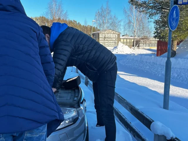 Tarvitaanko hiihtolomareissulla vikakoodinlukijaa? Entä savukonetta? Totta kai. Seistessäni hiihtolomareissulla Ruotsin Lyckselessä hampurilaisravintolan jonossa edessäni ollut mies kääntyi ympäri. Kyseessä olikin tuttuni, joten hetken hämmentyneen tuijottamisen ja tervehtimisen jälkeen hän kysyi: ”Onko sinulla vikakoodinlukija mukana?” Heidän Volvo XC90:nsä oli mennyt matkalla Hemavaniin vikatilaan (limp mode), jossa moottorin tehoa rajoitettiin. Mittaristossa näkyi ilmoitus Reduced performance.

Onneksi vikakoodinlukija oli mukana. En ollut alun perin edes ajatellut ottaa sitä hiihtolomalle mukaan, mutta kaveri, jolla on Volvo XC60, oli ennen reissua pyytänyt ottamaan sen varmuuden vuoksi mukaan.

Luetut vikakoodit näyttivät useita ilmamassamittariin (MAF) liittyviä koodeja sekä aliahtamiseen viittaavan koodin:

• P00BF00 – Mass Air Flow Sensor “B” Circuit Range/Performance (ilmamäärä poikkeaa odotetusta alueesta)
• P00BE00 – Mass Air Flow Sensor “B” Circuit Range/Performance (ilmamäärän signaali epärealistinen suhteessa moottorin tilaan)
• P029900 – Turbo/Supercharger Underboost Condition (turbo ei saavuta pyydettyä ahtopainetta)

MAF-anturi mittaa moottoriin tulevan ilman määrää. Sen perusteella moottorinohjaus säätää polttoaineen määrän ja seuraa, tuottaako turbo oikean määrän ahtopainetta. Aliahtaminen (underboost) tarkoittaa, että turbo ei saavuta pyydettyä ahtopainetta. Yleinen syy on ahtovuoto – paine karkaa ennen kuin se ehtii moottoriin. Silmämääräisesti ei löytynyt selvää halkeamaa ahtoputkista, mutta kokonaisuus viittasi vahvasti ahtopuolen ongelmaan. Katsoin myös livedataa, jossa MAF-anturi näytti tyhjäkäynnillä normaalista korkeampaa lukemaa, mikä sopi kuvaan siitä, että ilmamäärä tai ahtopaine ei käyttäytynyt kuten pitäisi. Auto ei kuitenkaan viheltänyt tai ujeltanut, mikä usein viittaisi ahtovuotoon. Oletettavasti repeämä ahtoputkessa oli sen verran suuri, että paine karkasi suoraan ulos ilman että siitä syntyi selkeää vihellystä. Valistunut arvaukseni oli siis ahtovuoto.

Samalla huomasin, että auton 12 V akun jännite oli poikkeuksellisen matala. Kun olin jo lähdössä jatkamaan matkaa, tuttuni huomasi vielä yhden ongelman: Volvon sähköinen käsijarru ei vapautunut. Astuin takaisin ulos autostani ja menin tutkimaan tilannetta. Yritin vapauttaa käsijarrun myös testerin kautta, mutta sekään ei auttanut. Lopulta jouduin jättämään heidät ja jatkamaan omaa matkaani, mikä tuntui siinä hetkessä aika ikävältä. Onneksi heillä oli kuitenkin mukana akkuboosteri – he tiesivät jo entuudestaan akun olevan heikko. Kun boosteri kytkettiin akkuun, käsijarru vapautui ja he pääsivät jatkamaan matkaa kohti Hemavania.

Pari päivää myöhemmin Hemavanissa tarkastelin asiaa vielä lisää. Tyhjäkäynnillä MAF näytti yli 15 g/s, mikä on selvästi korkea arvo lämpimälle moottorille (normaalisti noin 5–8 g/s). Irrotin MAF-anturin liittimen testiksi. Kun MAF kytketään irti, moottorinohjaus siirtyy käyttämään korvausarvoa eli varastrategiaa, jossa ilmamäärä lasketaan muiden antureiden, kuten imusarjapaineen ja kierrosluvun perusteella. Jos itse MAF olisi viallinen, moottorin käytös usein muuttuu selvästi tässä tilanteessa. Tässä tapauksessa merkittävää muutosta ei tullut, mikä vahvisti epäilyä siitä, ettei varsinainen vika ole itse anturissa vaan ilmamäärän todellisessa poikkeamassa.

Tarkistin samalla myös DPF-hiukkassuodattimen paine-eron, koska autoa oli ajettu pitkään rajoitetulla teholla. Tyhjäkäynnillä paine-ero oli yli 14 mbar – koholla oleva arvo. Epäilin hetken, voisiko tukkeutuva hiukkassuodatin aiheuttaa pakopuolen vastapainetta ja vaikuttaa turbon toimintaan. Kuitenkin lukemat eivät viitanneet vielä vakavaan tukkeumaan, ja kokonaisuus sopi paremmin ahtovuotoon kuin pakopuolen rajoitukseen. Kohonnut paine oli todennäköisemmin seurausta siitä, ettei regenerointi ollut limp-tilassa päässyt toteutumaan normaalisti.

Auton omistaja oli tässä vaiheessa myös käynyt ostamassa autoon uuden akun ja vaihtanut sen itse, joten lisädiagnostiikan yhteydessä koodasin uuden akun vielä autoon. Pohdimme vielä, kannattaisiko autolla yrittää ajaa noin 400 kilometrin matka kotiin vai toimittaa se korjaamolle Ruotsissa. Vaikka teknisesti autolla olisi todennäköisesti päässyt perille asti, minua huolestutti hiukkassuodattimen mahdollinen lisätukkeutuminen ja jopa vaurioituminen, jos matkaa jatkettaisiin pitkään vikatilassa. Lopulta Volvolle päätettiin tilata hinausauto ja se vietiin korjaamolle Lyckseleen. Perhe pääsi jatkamaan kotimatkaa sijaisautolla. Tuomio korjaamolla: haljennut ahtoputki välijäähdyttimeltä. Eli juuri se, mihin vikakoodit, livedata ja kokonaisuus kenttäolosuhteissa viittasivat ja mihin valistunut arvaukseni alun perin osoitti.

Seuraavalla kerralla otan myös savukoneen mukaan.

#autodiagnostiikkamies #McYnen

Behöver man en felkodsläsare på sportlovsresan? Och en rökmaskin? Självklart. När jag stod i kön på en hamburgerrestaurang i Lycksele i Sverige under sportlovsresan vände sig en man framför mig om. Det visade sig vara en bekant, så efter en stunds förvånat stirrande och ett hej frågade han: ”Har du felkodsläsaren med dig?” Deras Volvo XC90 hade gått in i nödläge (limp mode) på väg till Hemavan, vilket innebar att motoreffekten begränsades. I instrumentpanelen stod det Reduced performance.

Som tur var hade jag felkodsläsaren med mig. Från början hade jag inte ens tänkt ta med den på sportlovet, men en kompis som har en Volvo XC60 hade före resan bett mig ta med den för säkerhets skull.

De avlästa felkoderna visade flera koder relaterade till luftmängdsmätaren (MAF) samt en kod som tydde på för lågt laddtryck:

• P00BF00 – Mass Air Flow Sensor “B” Circuit Range/Performance (luftmängden avviker från det förväntade området)
• P00BE00 – Mass Air Flow Sensor “B” Circuit Range/Performance (luftmängdssignalen är orealistisk i förhållande till motorns driftläge)
• P029900 – Turbo/Supercharger Underboost Condition (turbon når inte det begärda laddtrycket)

MAF-sensorn mäter mängden luft som kommer in i motorn. Utifrån den informationen reglerar motorstyrningen bränslemängden och följer upp om turbon producerar rätt laddtryck. För lågt laddtryck (underboost) innebär att turbon inte når det begärda laddtrycket. En vanlig orsak är ett läckage i laddluftsystemet – trycket läcker ut innan luften når motorn. Vid en visuell kontroll hittade jag ingen tydlig spricka i laddluftsrören, men helhetsbilden pekade starkt på ett problem på laddluftssidan. Jag tittade också på livedata, där MAF-sensorn visade ett högre värde än normalt på tomgång, vilket passade in på att luftmängden eller laddtrycket inte betedde sig som det borde. Bilen visslade eller ylade dock inte, vilket ofta skulle tyda på ett läckage i laddluftsystemet. Förmodligen var sprickan i laddluftsröret så pass stor att trycket läckte rakt ut utan att ge upphov till något tydligt visslande ljud. Min kvalificerade gissning var alltså ett läckage i laddluftsystemet.

Samtidigt noterade jag att spänningen i bilens 12 V-batteri var ovanligt låg. När jag redan var på väg att fortsätta resan upptäckte min bekant ytterligare ett problem: Volvons elektriska parkeringsbroms släppte inte. Jag steg ur bilen igen och gick tillbaka för att undersöka situationen. Jag försökte även frigöra parkeringsbromsen via testern, men inte heller det hjälpte. Till slut var jag tvungen att lämna dem och fortsätta min egen resa, vilket kändes ganska tråkigt just då. Som tur var hade de ändå en batteribooster med sig – de visste sedan tidigare att batteriet var svagt. När boostern kopplades till batteriet släppte parkeringsbromsen och de kunde fortsätta resan mot Hemavan.

Ett par dagar senare i Hemavan undersökte jag saken lite närmare. På tomgång visade MAF över 15 g/s, vilket är ett klart högt värde för en varm motor (normalt cirka 5–8 g/s). Jag kopplade loss kontakten till MAF-sensorn som ett test. När MAF kopplas bort övergår motorstyrningen till att använda ett ersättningsvärde, alltså en reservstrategi där luftmängden beräknas utifrån andra sensorer, såsom insugningstrycket och motorvarvtalet. Om själva MAF-sensorn hade varit defekt förändras motorns beteende ofta tydligt i den här situationen. I det här fallet blev det ingen märkbar förändring, vilket stärkte misstanken om att det egentliga felet inte låg i själva sensorn utan i en verklig avvikelse i luftmängden.

Jag kontrollerade samtidigt även differenstrycket över DPF-partikelfiltret, eftersom bilen hade körts en längre sträcka med begränsad effekt. På tomgång låg differenstrycket på över 14 mbar – ett förhöjt värde. Jag funderade en stund på om ett partikelfilter som började bli tilltäppt kunde orsaka mottryck på avgassidan och påverka turbons funktion. Värdena tydde dock ännu inte på att partikelfiltret var allvarligt tilltäppt, och helhetsbilden stämde bättre överens med ett läckage i laddluftsystemet än med en begränsning på avgassidan. Det förhöjda trycket var sannolikt snarare en följd av att regenereringen inte hade kunnat genomföras normalt när bilen befann sig i nödläge.

Bilens ägare hade vid det här laget också varit och köpt ett nytt batteri och bytt det själv, så i samband med den fortsatta diagnostiken kodade jag även in det nya batteriet i bilen. Vi funderade ännu på om det var värt att försöka köra den cirka 400 kilometer långa vägen hem eller om bilen skulle lämnas till en verkstad i Sverige. Även om bilen tekniskt sett sannolikt hade kunnat ta sig hela vägen hem, oroade jag mig för att partikelfiltret skulle kunna bli ännu mer tilltäppt och till och med skadas om man fortsatte köra en längre sträcka i nödläge. Till slut bestämde de sig för att beställa en bärgningsbil till Volvon och den transporterades till en verkstad i Lycksele. Familjen kunde fortsätta hemresan med en ersättningsbil. Domen från verkstaden: ett sprucket laddluftsrör från intercoolern. Alltså precis det som felkoderna, livedatan och helhetsbilden under fältförhållandena pekade på och det som min kvalificerade gissning ursprungligen hade landat i.

Nästa gång tar jag också med rökmaskinen.

#bildiagnostikmannen #McYnen